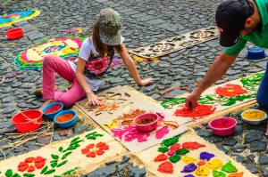 Antigua, Guatemala - March 22, 2015: Local father & daughter decorate cross shaped carpet with floral pattern of dyed sawdust using cardboard stencils for Lent procession to walk over on cobblestone street in colonial town with most famous Holy Week celebrations in Latin America.